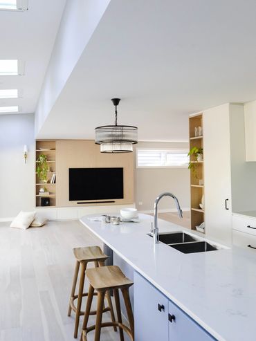 Light-filled white coastal kitchen with blue island, and oak shelving