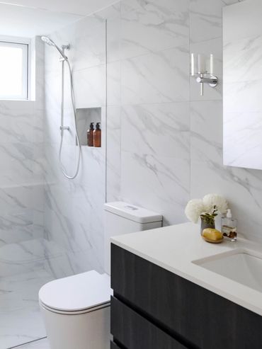 Modern marble bathroom with frameless shower screen, glass wall-lights, and dark timber vanity