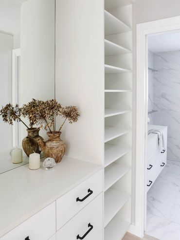 light-filled modern wardrobe with black handles. Marble bathroom beyond.