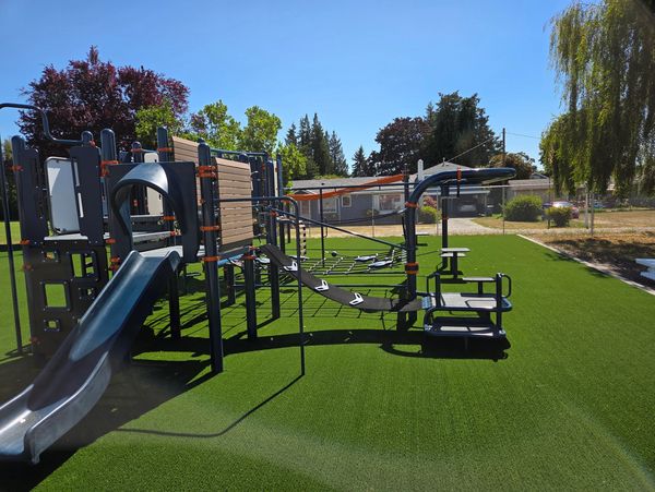 Modern playground with slide and climbing structures on green turf under clear blue sky.