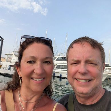 Happy couple smiling by the marina with yachts in the background.