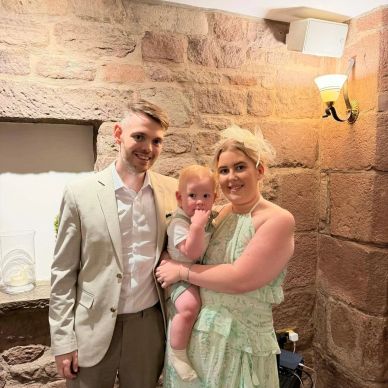 A family portrait with a man, woman, and baby indoors.