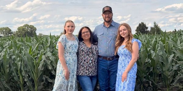 Family of four standing in front of a cornfield.