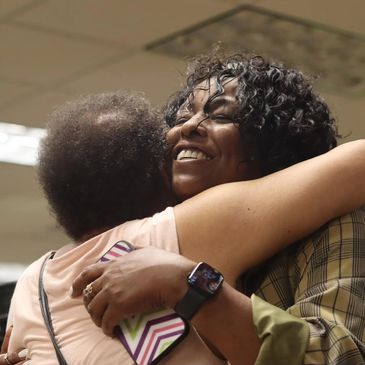 Two women warmly embrace, sharing a joyful moment indoors.