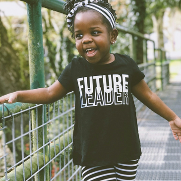 Smiling toddler in black and white outfit standing on a metal walkway outdoors.