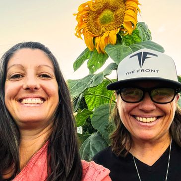 Two smiling people posing with a large sunflower in the background.