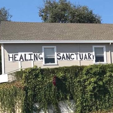 House with 'Healing Sanctuary' sign on its side above greenery.