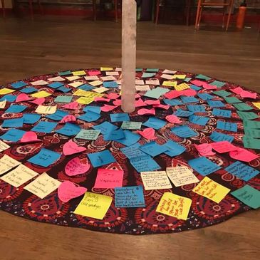 Colorful sticky notes arranged in a circular pattern on a patterned cloth around a wooden pole.