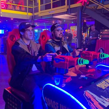 Two men playing arcade shooting game with neon lights.