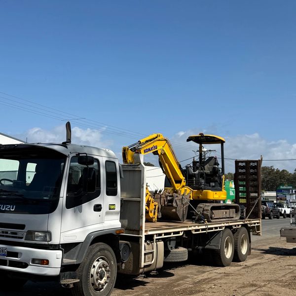 A white truck carrying a yellow Komatsu excavator.