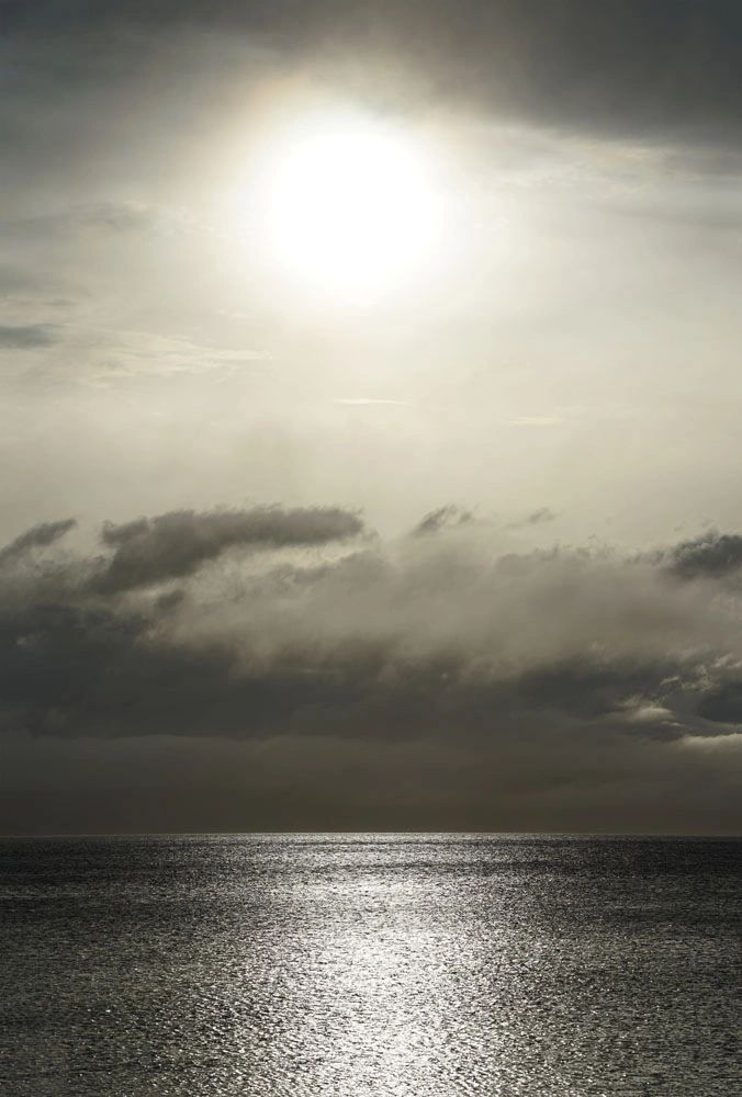 Sun shining through clouds over a calm sea.