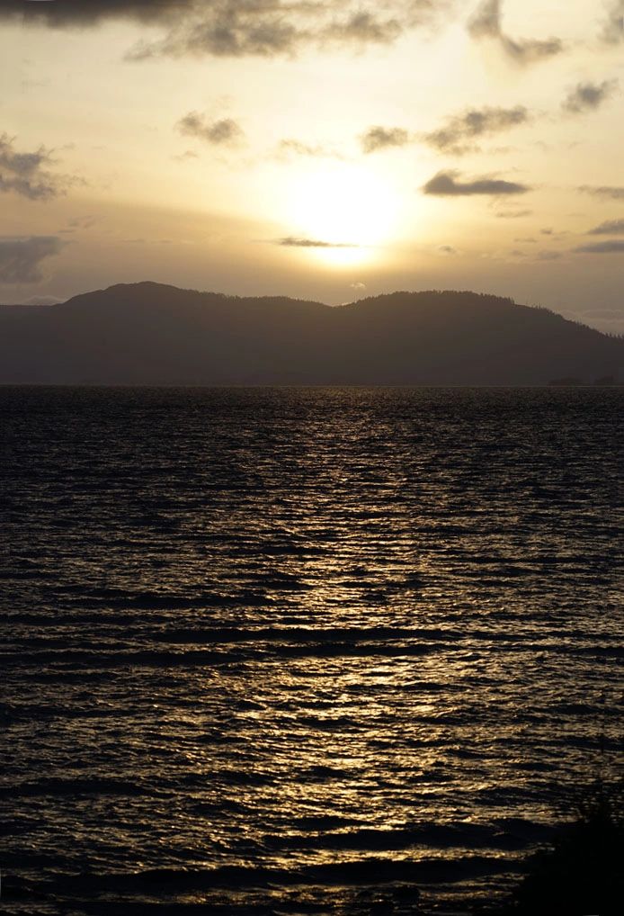 Sunset over a calm sea with silhouetted hills in the background.