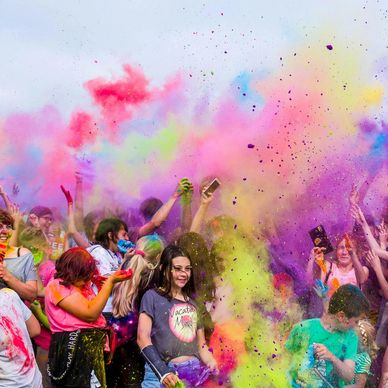 A vibrant crowd joyfully throwing colored powder at a lively festival.