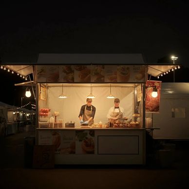 Two vendors prepare food at a warmly lit night market stall.