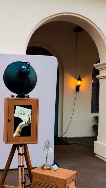 Photo booth setup with wooden frame and modern lamp outside an arched building entrance.