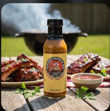 A bottle of barbecue sauce with grilled ribs and a bowl of sauce outdoors.