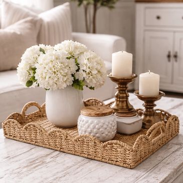 Decorative tray with white flowers, candles, and jars on a wooden table.