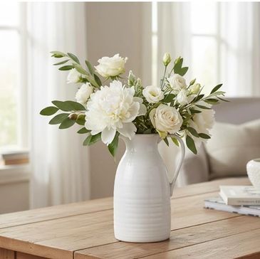 Elegant white flowers arranged in a white vase on a wooden table.