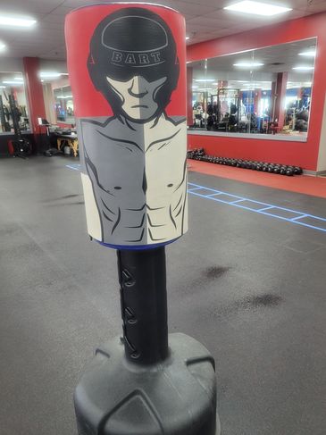 A boxing training dummy with a muscular figure and helmet labeled 'BART' in a gym.