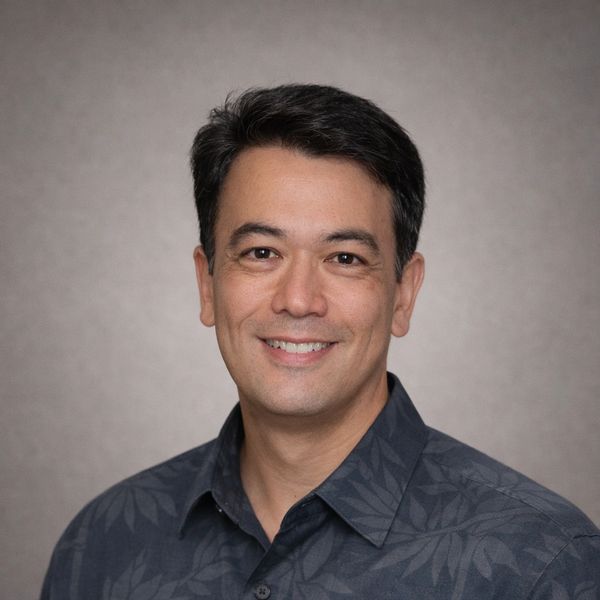 Smiling man in a dark patterned shirt.