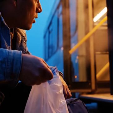 A person holding a plastic bag near a bus entrance at dusk.