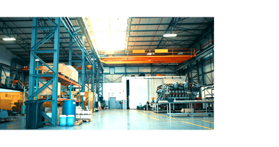 Spacious industrial warehouse with machinery, storage shelves, and overhead crane system.