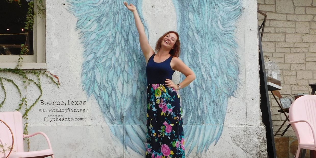 Woman posing with painted angel wings mural in Boerne, Texas.