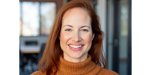 Smiling woman in orange sweater in an office setting.