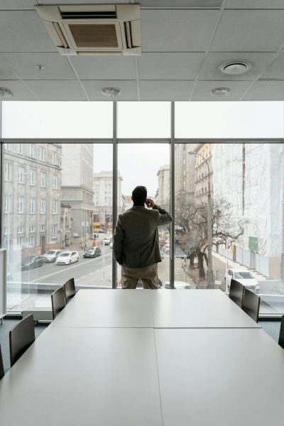 Man in office looking out large window at city street.