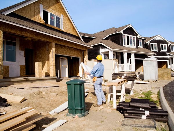 A man in a hard hat looking at blueprints at a residential construction site.