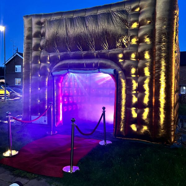 Inflatable golden entrance with purple lights and red carpet at dusk.