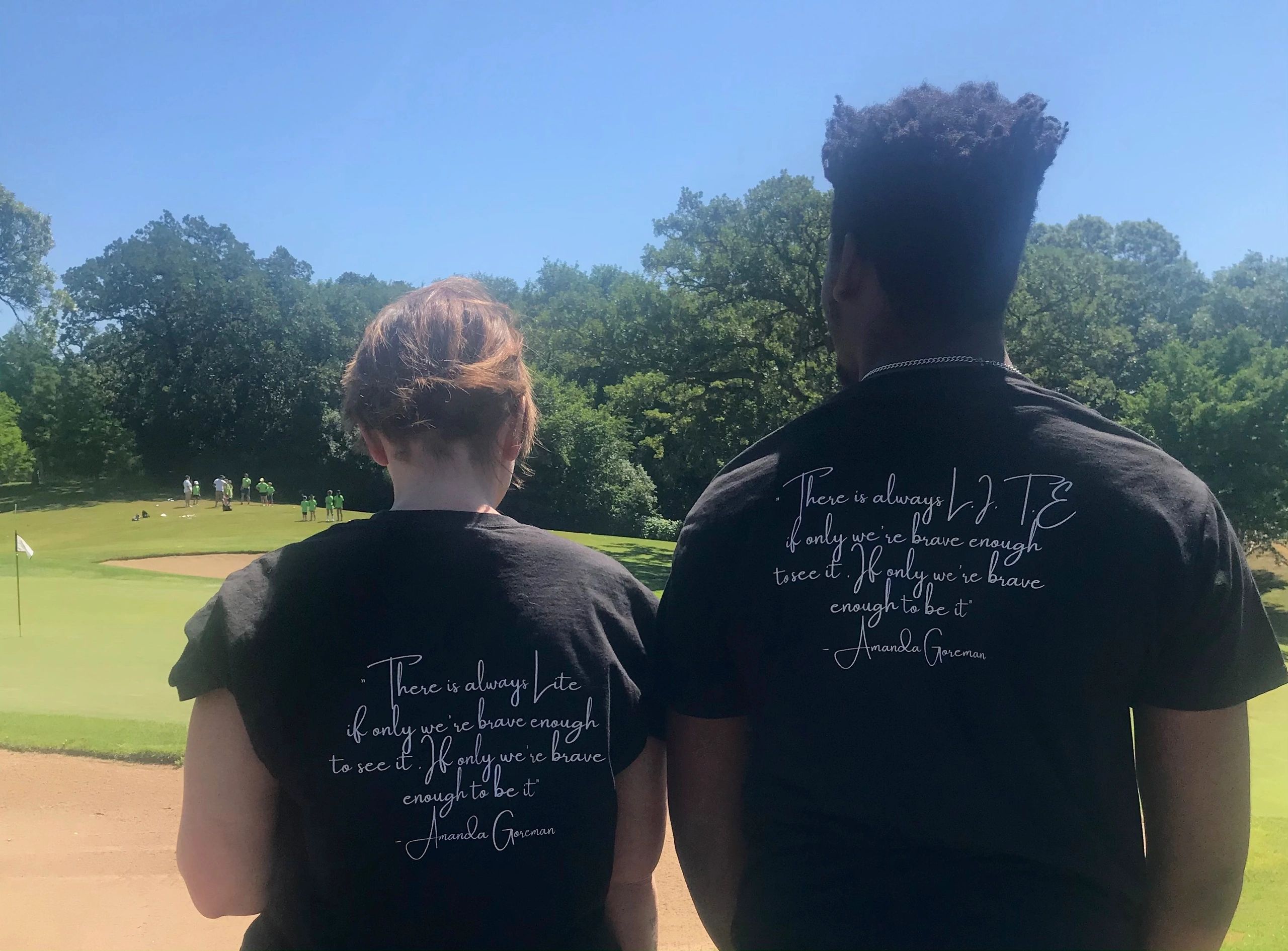 Two people standing on a golf course wearing matching quote t-shirts.