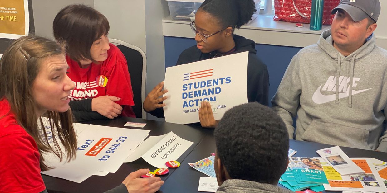 Group discussing gun control advocacy with signs and pamphlets.