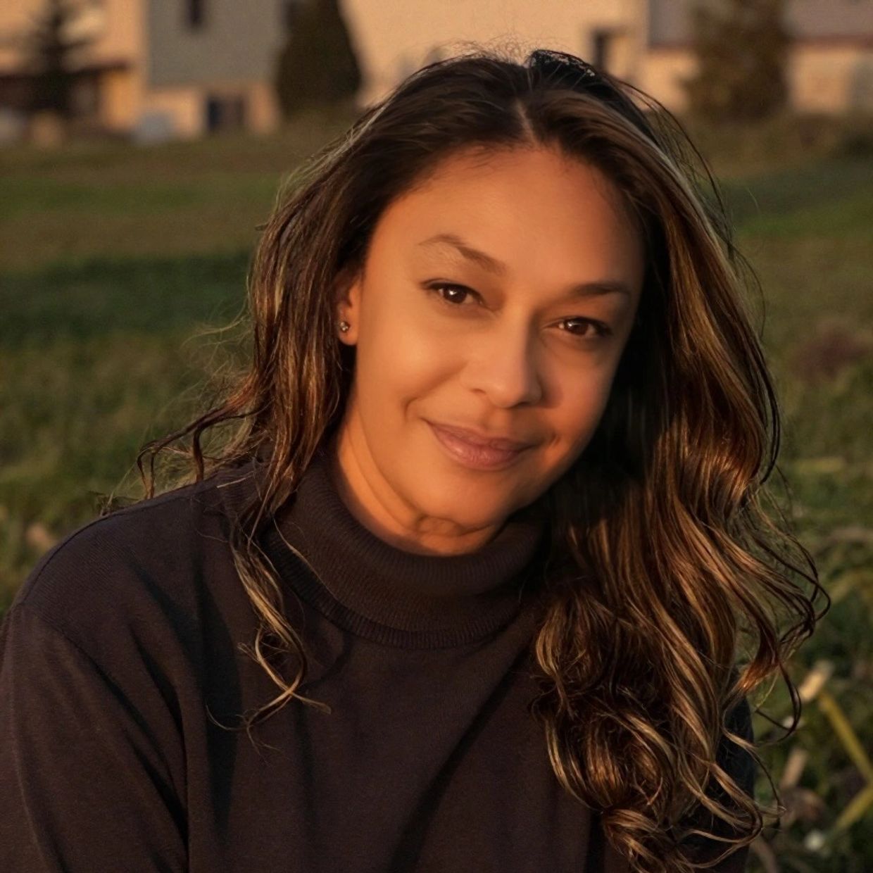 Woman with long hair smiling warmly outdoors at sunset.