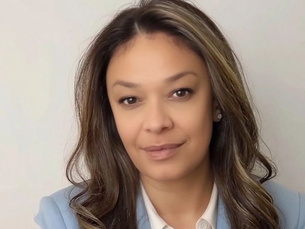 A woman with long brown hair wearing a light blue blazer and white shirt.