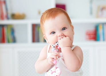 A red-headed infant is chewing on a toy.
