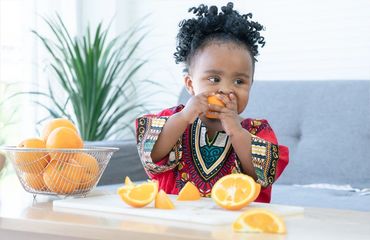 A black/African American toddler eating oranges.