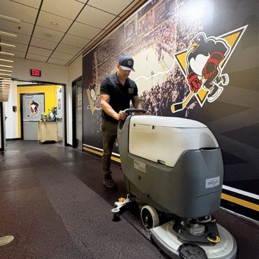 A man cleaning a hallway with a floor scrubber near Pittsburgh Penguins logos.