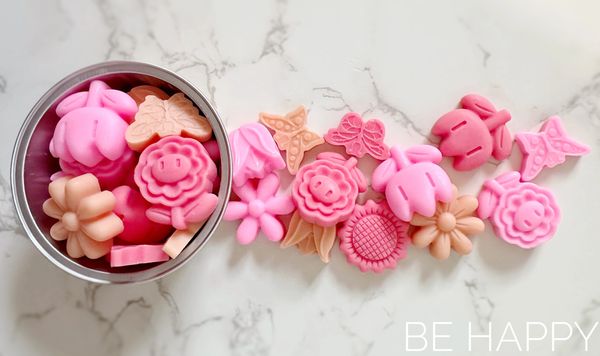 Round container filled with small pink and coral scented wax melts. Butterfly and Flower shaped.