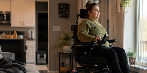 Woman in a wheelchair looking out of a window with a smile.