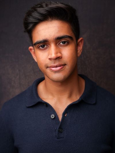 Portrait of a young man in a dark collared shirt against a dark background.