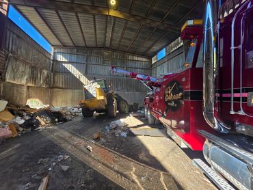 Heavy-duty garage truck towing a large yellow bulldozer inside a cluttered warehouse.