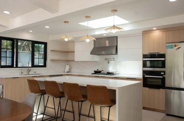 Modern kitchen with white countertops, wooden cabinets, and brown bar stools.