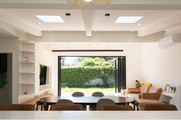 Bright dining room with open doors to a green garden and cozy seating.