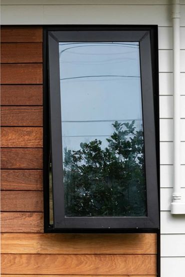 A modern window with black frame on mixed wood and white siding exterior.