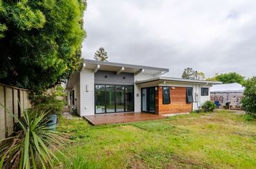 Modern single-story house with large windows and a spacious backyard.
