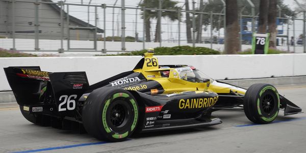 Yellow and black IndyCar with number 26 in a pit lane area.