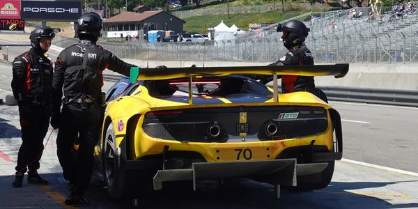 Yellow Ferrari race car in the pit stop with crew members.