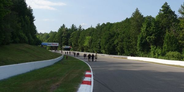 People walking on a race track surrounded by greenery under a blue sky.