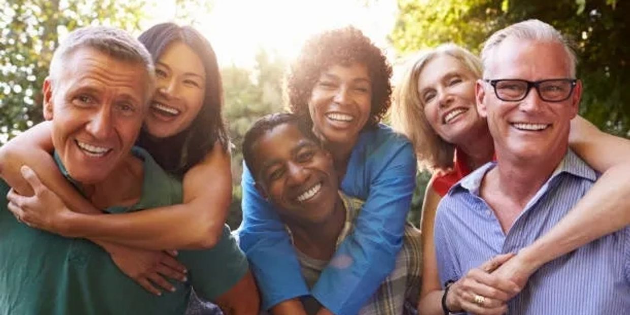 Group of diverse friends smiling and hugging outdoors in sunlight.